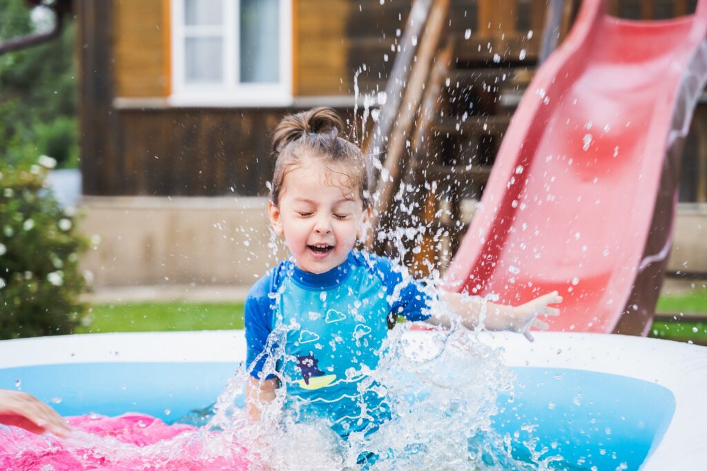 Staycation.Little girl in swimsuit swim,rolls down slide Inflatable rubber pool.Home summer activity